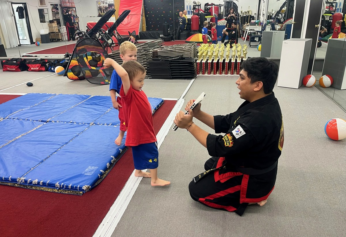 An instructor working with a student at mat level during a martial arts class.